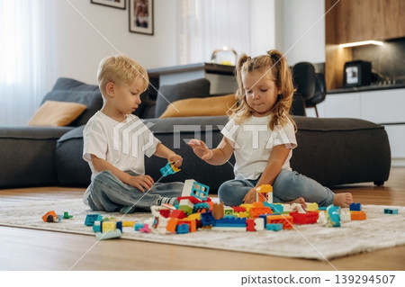Building the tower, sitting. Two kids are playing with construction blocks toys at home 139294507