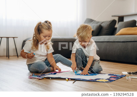 On the floor, learning how to draw. Little kids are playing together in the domestic room at daytime On the floor, learning how to draw. Little kids are playing together in the domestic room at daytime 139294528