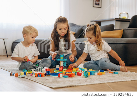 Improving the motor skills. Three kids are playing with construction blocks toys at home together Improving the motor skills. Three kids are playing with construction blocks toys at home together 139294633