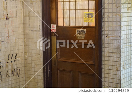 A scene reminiscent of Kowloon Walled City, with graffiti-covered tiled walls and old wooden doors. 139294859