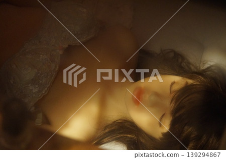A realistic female mannequin wearing lace lingerie lies in warm light. A realistic female mannequin wearing lace lingerie lies in warm light. 139294867