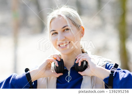Smiling blonde woman holding headphones around her neck in a park 139295256