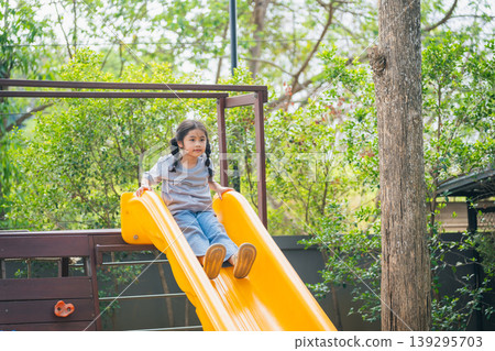 Joyful Child Playing on Bright Yellow Slide in Green Backyard During Sunny Day, Enjoying Outdoor Fun and Adventure with Nature Surrounding Joyful Child Playing on Bright Yellow Slide in Green Backyard During Sunny Day, Enjoying Outdoor Fun and Adventure with Nature Surrounding 139295703