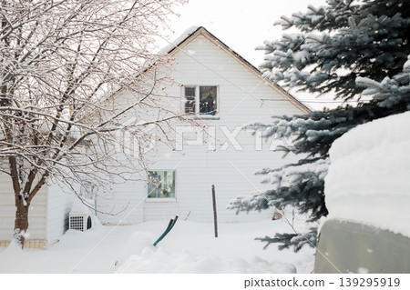 White house blanketed in pristine snow against a clear sky with evergreen and bare trees framing the winter scene. 139295919