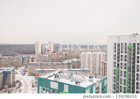 A panoramic view captures a snowy landscape of residential buildings, roads, and distant structures blanketed in white, winter's chill in an urban setting. Aerial view, city panorama 139296010