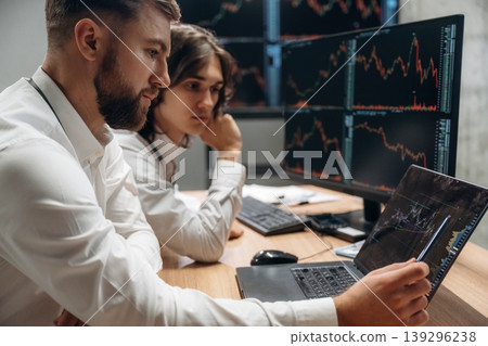 Modern laptop, bunch of displays. Two male exchange workers are in the office together Modern laptop, bunch of displays. Two male exchange workers are in the office together 139296238