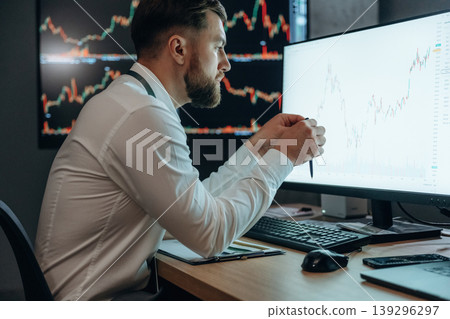 View from the side, sitting and looking at displays. Handsome businessman is in the office with stock exchange market information on displays 139296297