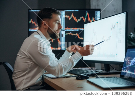 View from the side, sitting and looking at displays. Handsome businessman is in the office with stock exchange market information on displays 139296298