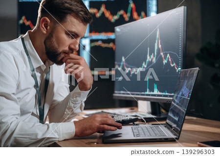 Handsome businessman is in the office with stock exchange market information on displays 139296303