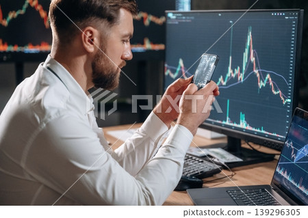 Handsome businessman is in the office with stock exchange market information on displays Handsome businessman is in the office with stock exchange market information on displays 139296305