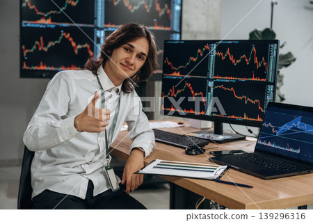 Real time monitoring graphs are on the screens. Young man is sitting in the office with multiple displays of stock market data Real time monitoring graphs are on the screens. Young man is sitting in the office with multiple displays of stock market data 139296316