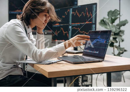 Real time monitoring graphs are on the screens. Young man is sitting in the office with multiple displays of stock market data 139296322