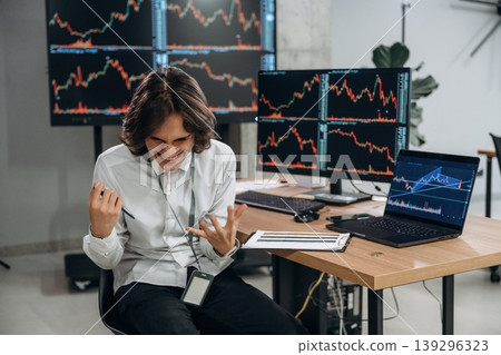 Young man is sitting in the office with multiple displays of stock market data Young man is sitting in the office with multiple displays of stock market data 139296323
