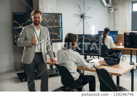 Looking at the camera, CEO is standing. Business people are working with stock market exchange in office 139296746