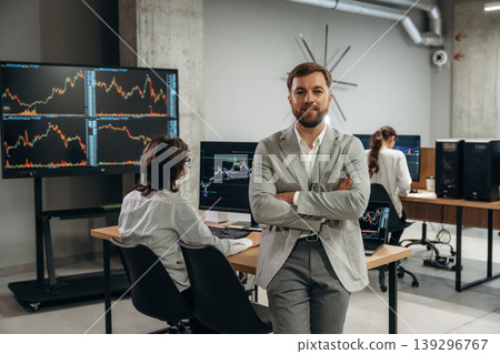 Arms crossed, man is standing. Business people are working with stock market exchange in office Arms crossed, man is standing. Business people are working with stock market exchange in office 139296767