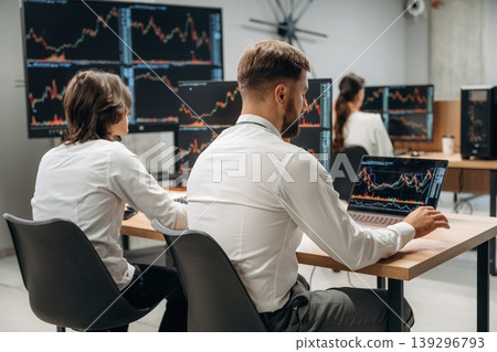 By the table, sitting. Business people are working with stock market exchange in office By the table, sitting. Business people are working with stock market exchange in office 139296793