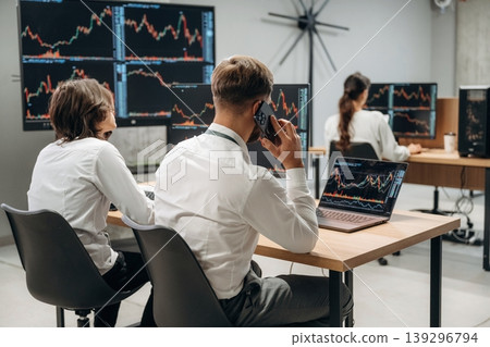 By the table, sitting. Business people are working with stock market exchange in office By the table, sitting. Business people are working with stock market exchange in office 139296794