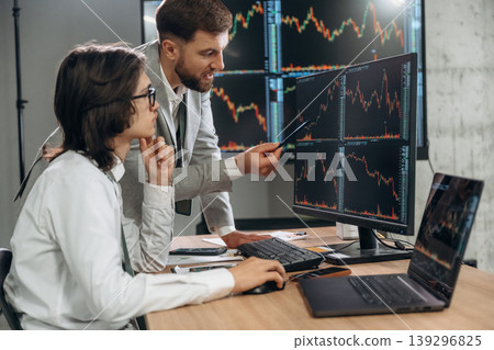 In formal clothes, by laptop and monitors. Two male exchange workers are in the office together 139296825