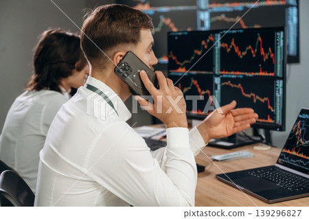 Making a call, talking by a phone. Two male exchange workers are in the office together Making a call, talking by a phone. Two male exchange workers are in the office together 139296827