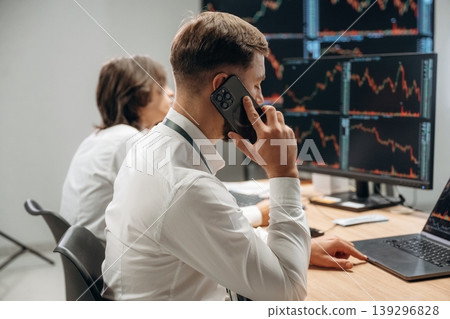 Making a call, talking by a phone. Two male exchange workers are in the office together Making a call, talking by a phone. Two male exchange workers are in the office together 139296828