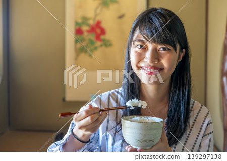 A young woman smiling while eating a meal at a traditional Japanese inn. A young woman smiling while eating a meal at a traditional Japanese inn. 139297138
