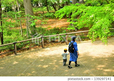 A parent and child taking a walk, bathed in sunlight filtering through the fresh green trees. A parent and child taking a walk, bathed in sunlight filtering through the fresh green trees. 139297141