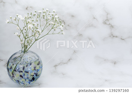 A single cool-toned glass sphere containing baby's breath flowers is arranged in a vase against a bright background (placed on the left). A single cool-toned glass sphere containing baby's breath flowers is arranged in a vase against a bright background (placed on the left). 139297160