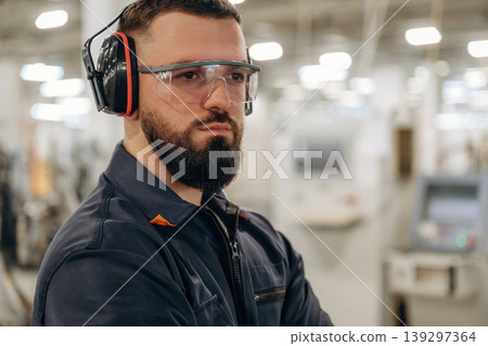 Posing, standing in protective eyewear. Warehouse worker in an industrial environment of a factory or storage area Posing, standing in protective eyewear. Warehouse worker in an industrial environment of a factory or storage area 139297364