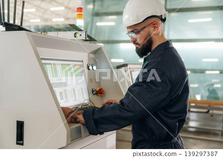 Side view, machine operator is standing and working. Warehouse worker in an industrial environment of a factory or storage area Side view, machine operator is standing and working. Warehouse worker in an industrial environment of a factory or storage area 139297387