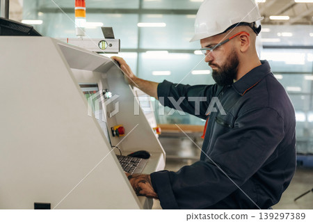 Side view, machine operator is standing and working. Warehouse worker in an industrial environment of a factory or storage area Side view, machine operator is standing and working. Warehouse worker in an industrial environment of a factory or storage area 139297389