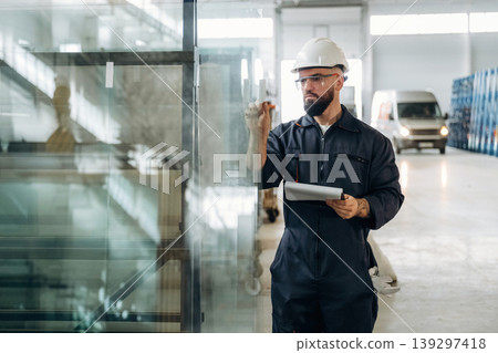 Quality control of the glass for windows. Warehouse worker in an industrial environment of a factory or storage area 139297418
