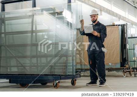 Quality control of the glass for windows. Warehouse worker in an industrial environment of a factory or storage area Quality control of the glass for windows. Warehouse worker in an industrial environment of a factory or storage area 139297419