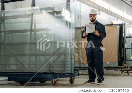 Quality control of the glass for windows. Warehouse worker in an industrial environment of a factory or storage area Quality control of the glass for windows. Warehouse worker in an industrial environment of a factory or storage area 139297420