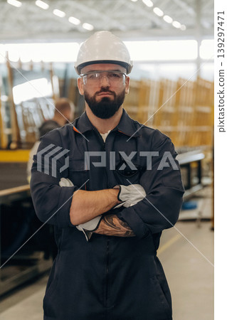 Arms crossed, standing. Warehouse worker in an industrial environment of a factory or storage area Arms crossed, standing. Warehouse worker in an industrial environment of a factory or storage area 139297471
