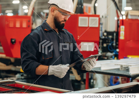 Notepad with document is in hands. Warehouse worker in an industrial environment of a factory or storage area Notepad with document is in hands. Warehouse worker in an industrial environment of a factory or storage area 139297479