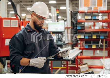 Notepad with document is in hands. Warehouse worker in an industrial environment of a factory or storage area Notepad with document is in hands. Warehouse worker in an industrial environment of a factory or storage area 139297512