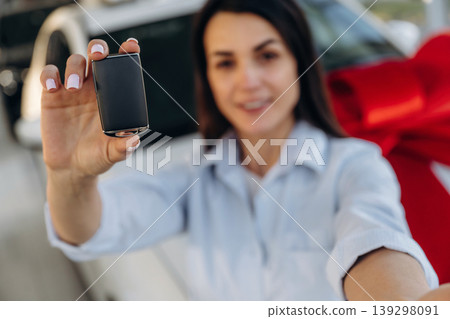 Expensive gift, present. Woman posing with a car in an auto showroom, modern dealership environment 139298091