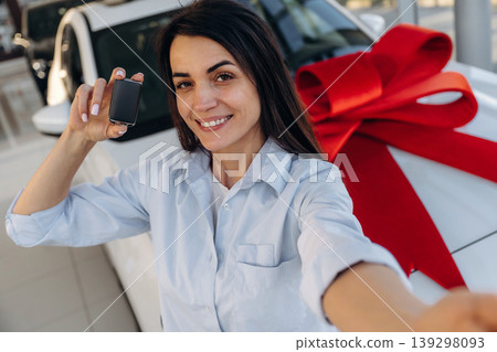 Expensive gift, present. Woman posing with a car in an auto showroom, modern dealership environment 139298093
