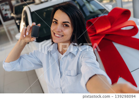 Expensive gift, present. Woman posing with a car in an auto showroom, modern dealership environment Expensive gift, present. Woman posing with a car in an auto showroom, modern dealership environment 139298094