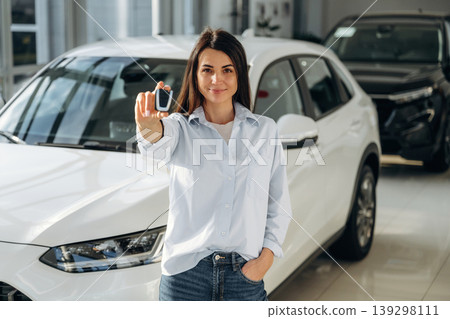 Ready to drive, showing keys. Woman posing with a car in an auto showroom, modern dealership environment 139298111