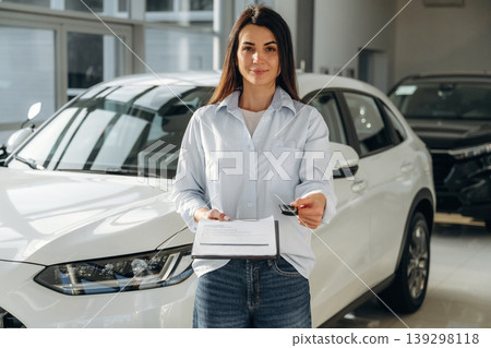 Brand new vehicle. Woman posing with a car in an auto showroom, modern dealership environment 139298118