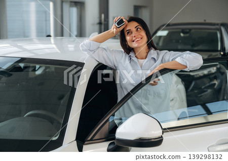 Smiling, happy new owner. Woman posing with a car in an auto showroom, modern dealership environment 139298132