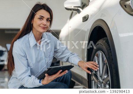 Woman posing with a car in an auto showroom, modern dealership environment Woman posing with a car in an auto showroom, modern dealership environment 139298413