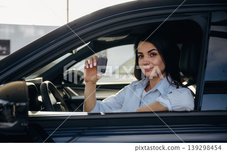 Showing the keys that are in hand. Woman is sitting in the modern car, happy new owner Showing the keys that are in hand. Woman is sitting in the modern car, happy new owner 139298454