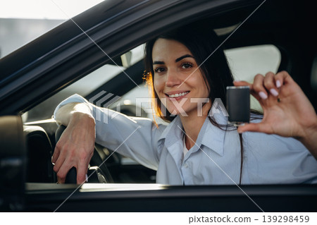 Through the window, holding keys. Woman is sitting in the modern car, happy new owner Through the window, holding keys. Woman is sitting in the modern car, happy new owner 139298459