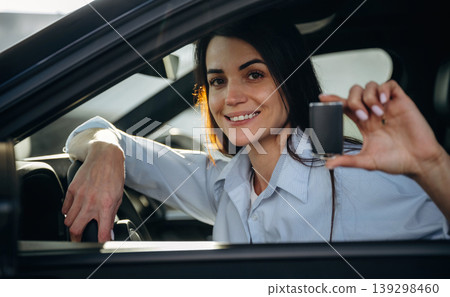 Through the window, holding keys. Woman is sitting in the modern car, happy new owner Through the window, holding keys. Woman is sitting in the modern car, happy new owner 139298460