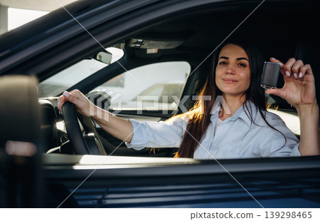 Proud owner is holding the keys. Woman is sitting in the modern car, happy new owner Proud owner is holding the keys. Woman is sitting in the modern car, happy new owner 139298465