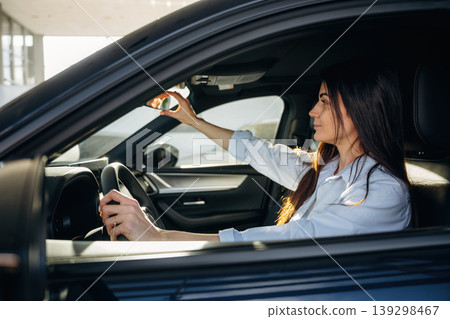 Adjusting the mirror. Woman is sitting in the modern car, happy new owner 139298467