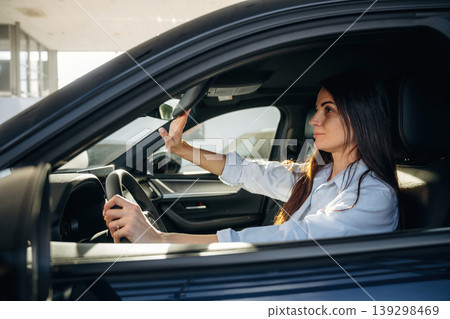Adjusting the mirror. Woman is sitting in the modern car, happy new owner Adjusting the mirror. Woman is sitting in the modern car, happy new owner 139298469