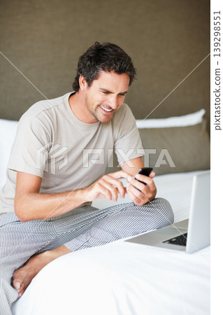 Phone, social media and laptop with a man in the bedroom of his home to relax on weekend time off. Tech, communication and person sitting on a bed while streaming a movie or series for entertainment Phone, social media and laptop with a man in the bedroom of his home to relax on weekend time off. Tech, communication and person sitting on a bed while streaming a movie or series for entertainment 139298551